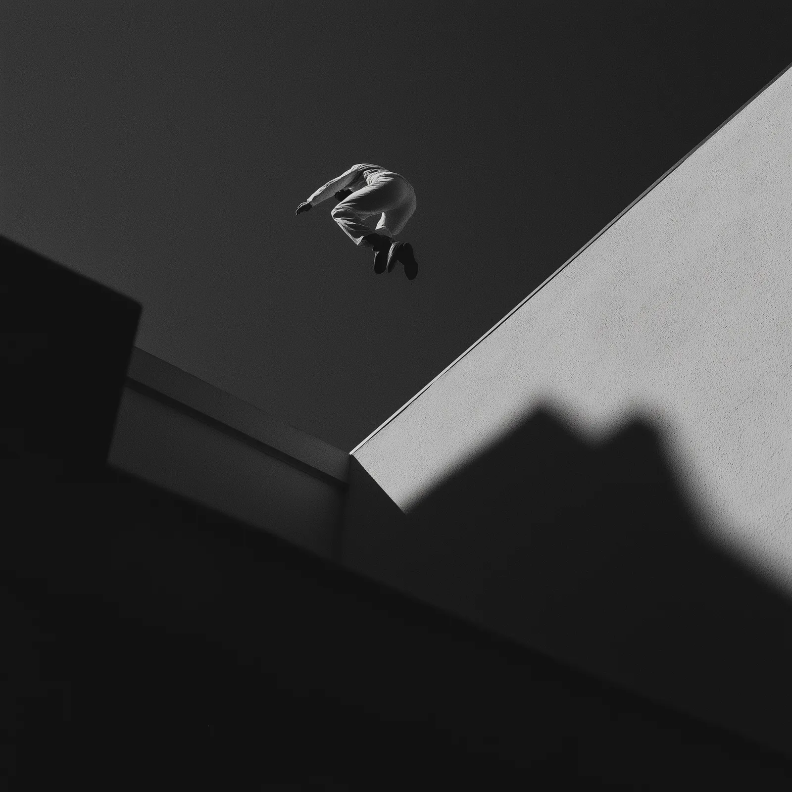 Black-and-white photograph of a person leaping above a stepped concrete edge